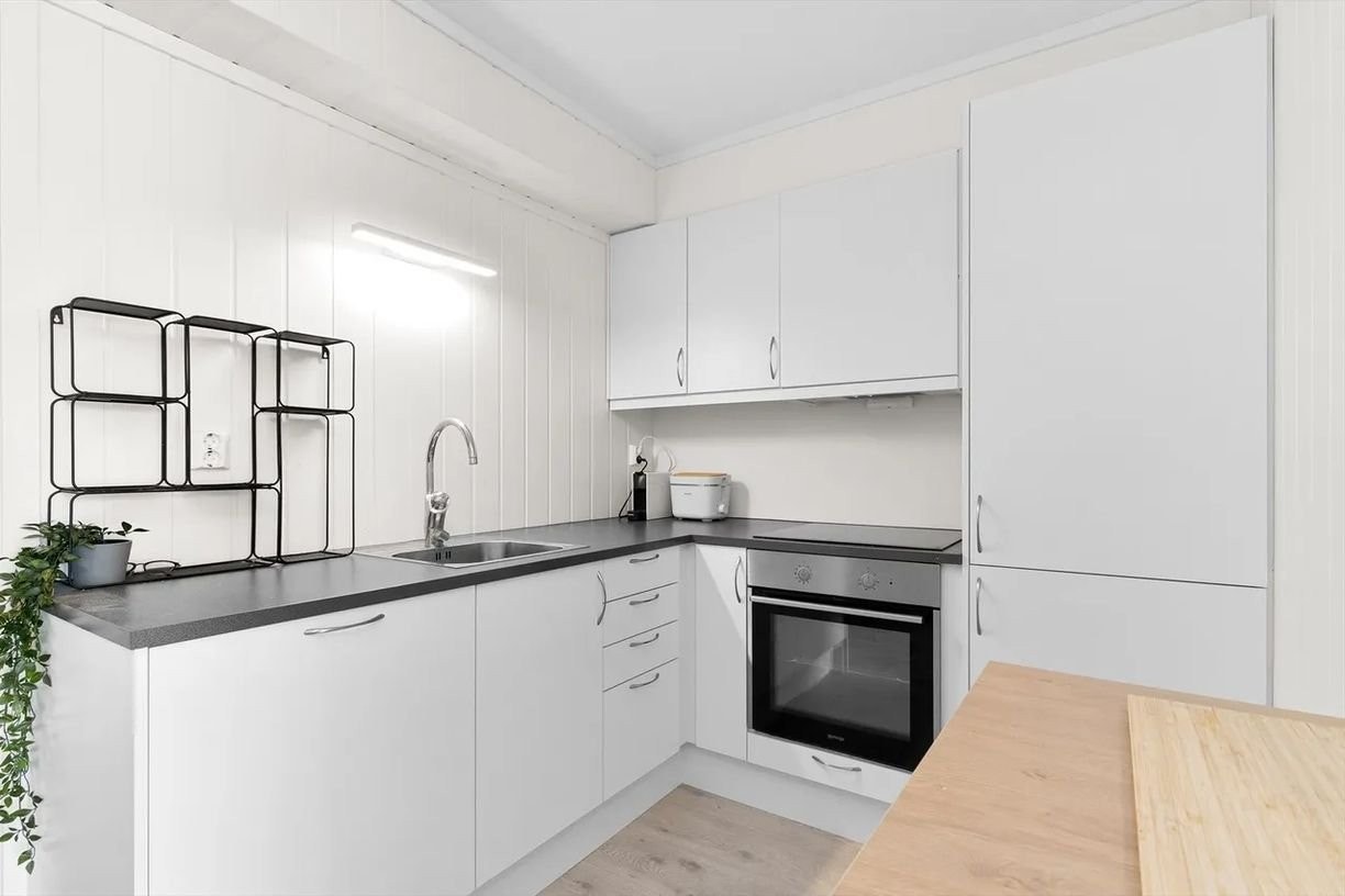 Stilrent og funksjonelt kjøkken med god skapplass, integrerte hvitevarer og benkeplate i mørk kontrast – en effektiv arbeidsflate for matlaging. Galleribilde