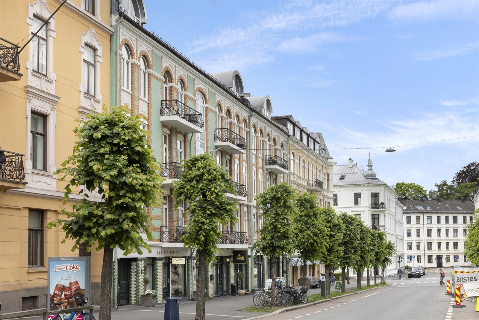 Gaten er lite trafikkert og omgitt av klassiske bygårder og grønne trekroner. Galleribilde