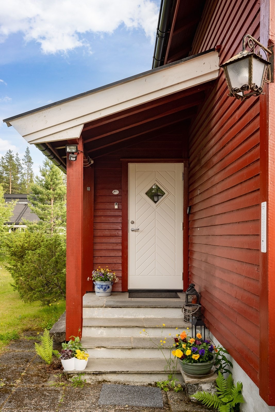 Du ønskes velkommen inn via et hyggelig overbygget inngangsparti med støpt trapp belagt med steinfliser. Malt ytterdør med glassfelt fra 2021. Galleribilde