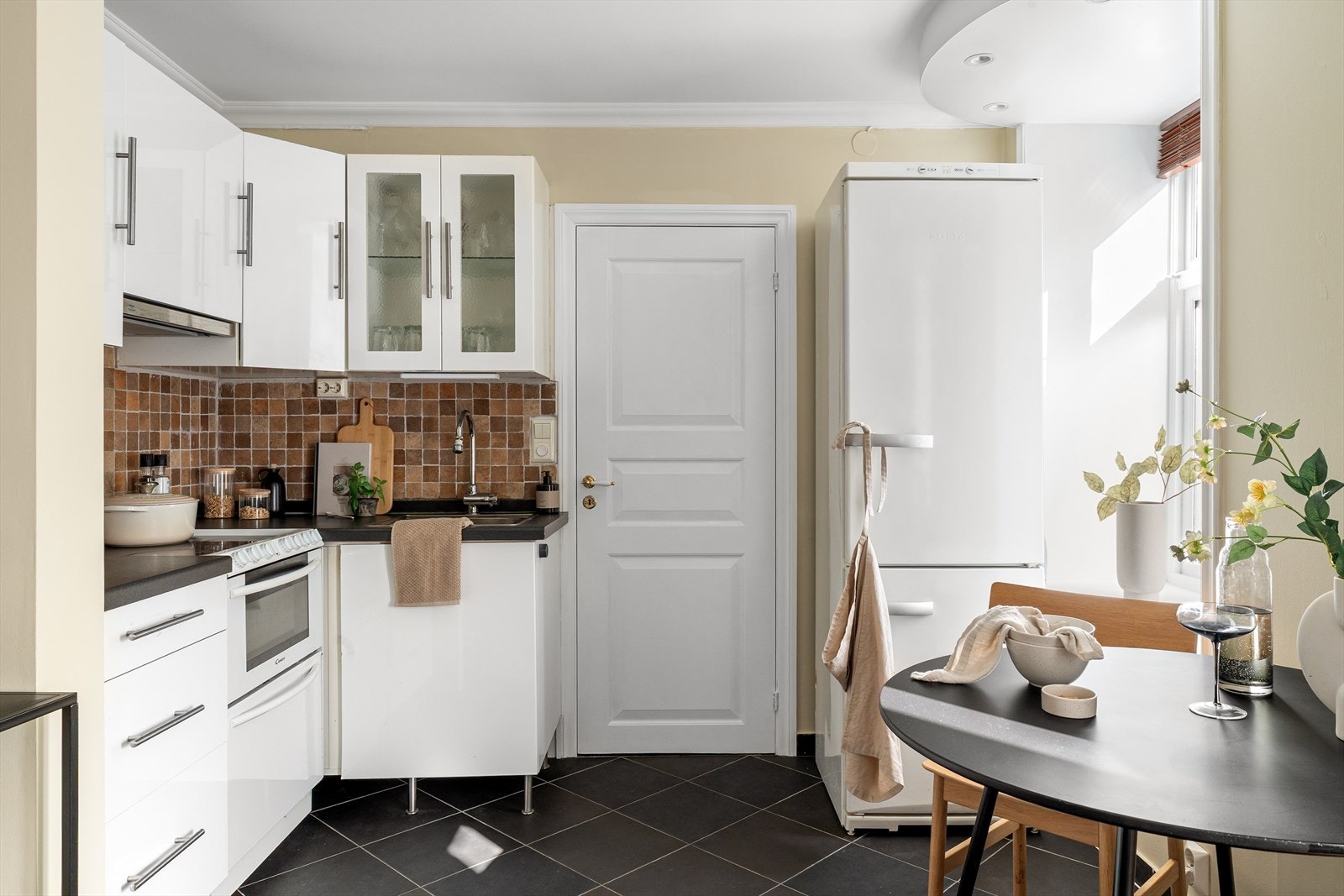 IKEA-kjøkken med hvite slette fronter og mørk laminat benkeplate med fliser over. Galleribilde