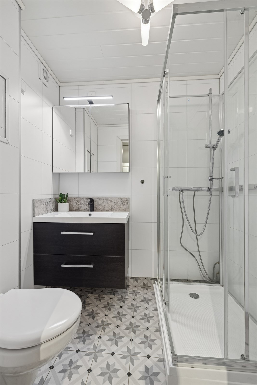 Badet kommer med servant i innredning, vegg-montert toalett og dusjkabinett Galleribilde