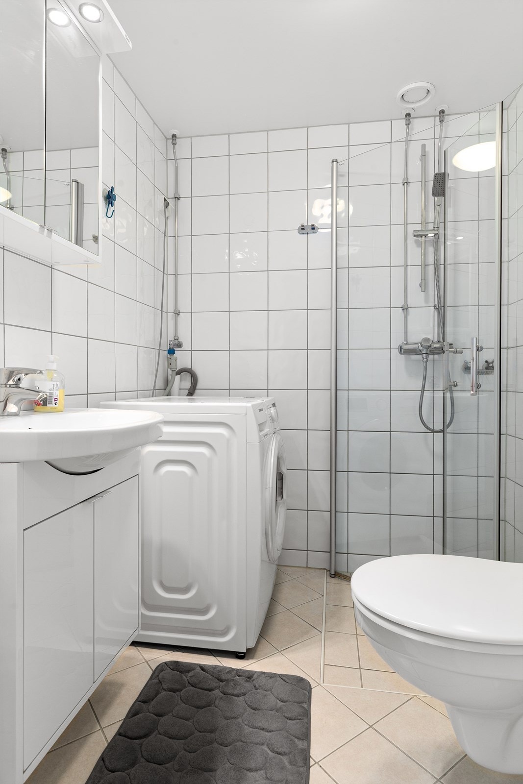 Pent flislagt bad med varmekabler i gulv og innredning bestående av vegghengt klosett, dusjhjørne med innfellbare dører og baderomsinnredning. Opplegg for vaskemaskin Galleribilde