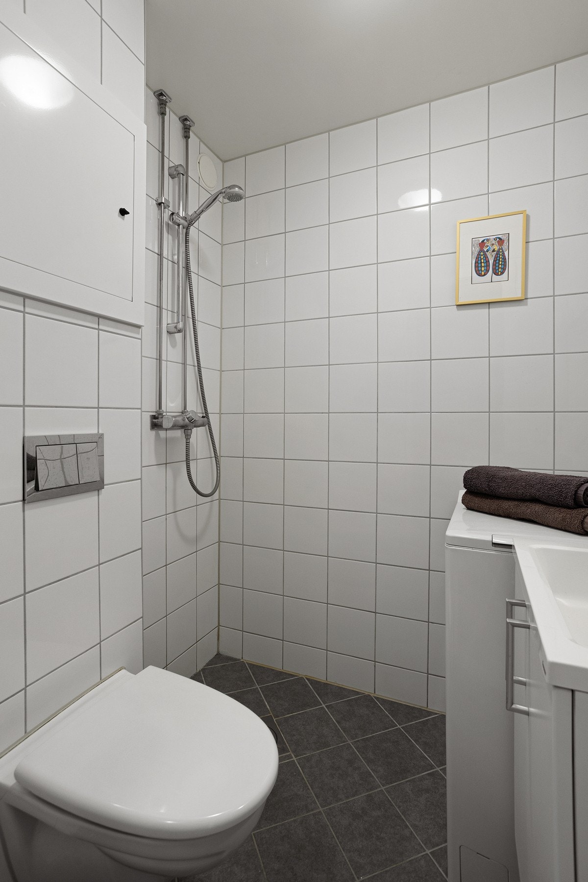 Baderomsinnredningen er bestående av skap med servant, vegghengt toalett og åpen dusjsone med dusjarmatur. Galleribilde