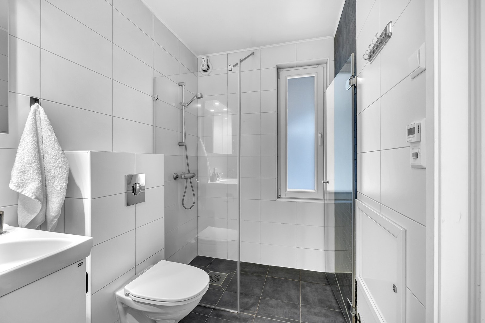 Videre består innredningen av veggmontert toalett, dusjhjørne samt servant med underskap som gir praktisk oppbevaringsplass. Galleribilde