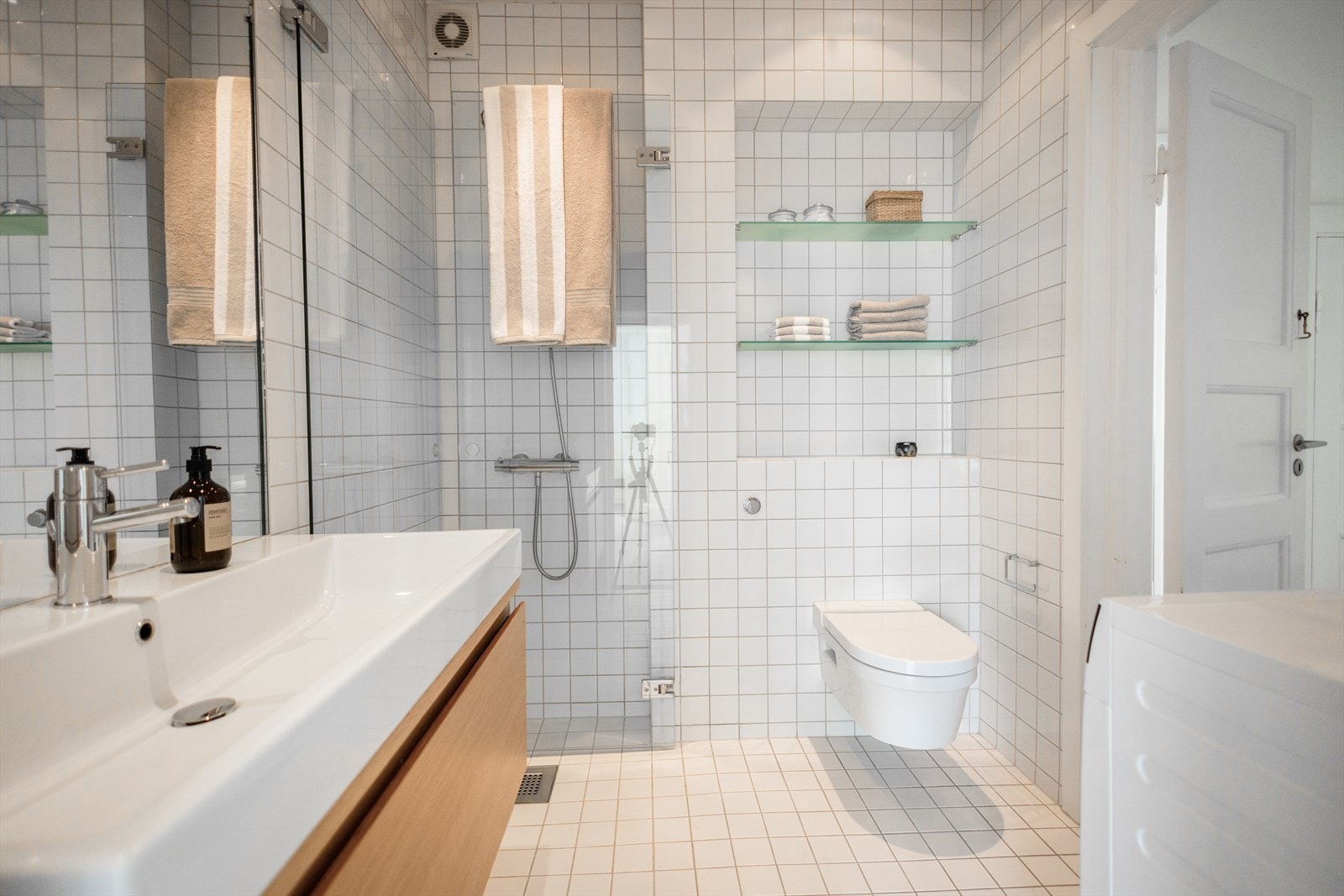 Badet er utstyrt med innfellbare dusjdører, opplegg for vaskemaskin, servantskap og veggmontert wc Galleribilde