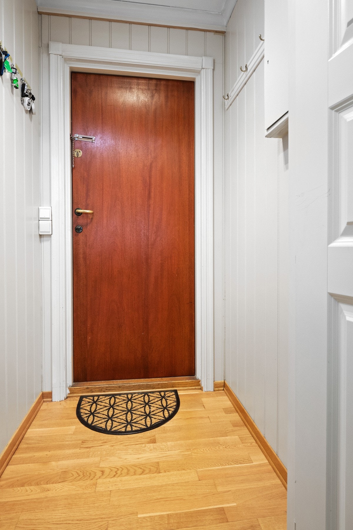 Vindfanget på innsiden har parkettgulv, hvitmalte panelvegger og knagger på én vegg. Galleribilde