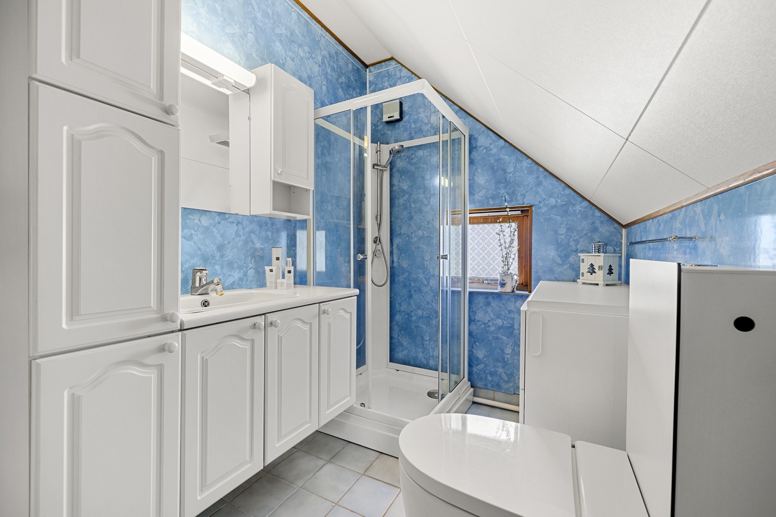 Badet har dusjkabinett, vegghengt toalett og praktisk innredning med nedfelt servant. Galleribilde