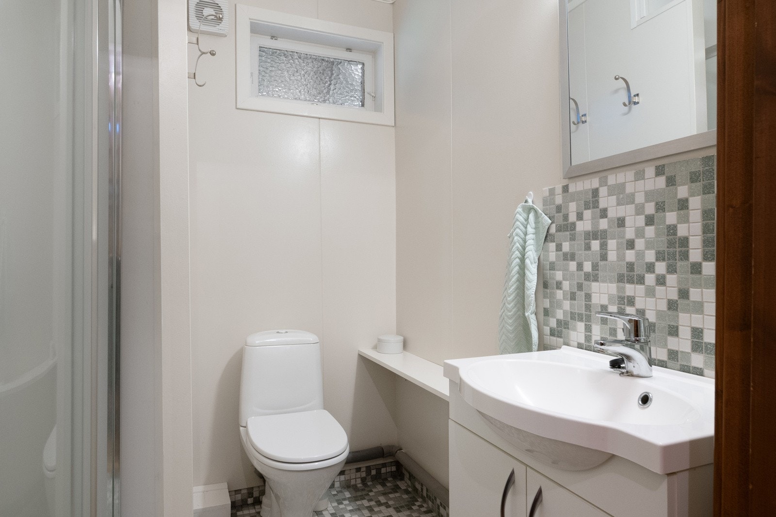 Badet har enkel innredning med servantskap, gulvmontert toalett, speil og dusjdører. Galleribilde