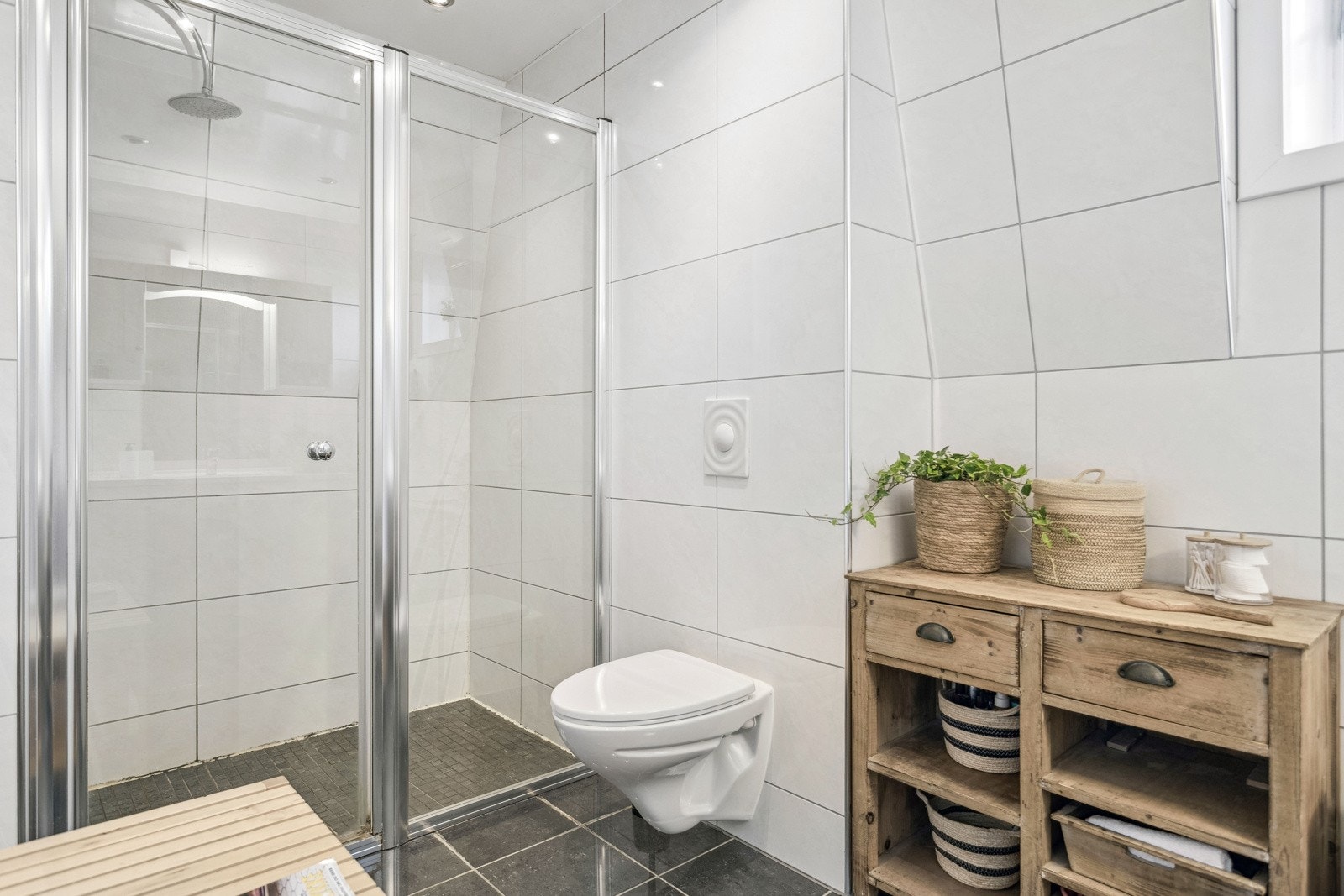 Det er utstyrt med vegghengt servantinnredning, dusjnisje med glassvegger, vegghengt toalett, og praktiske detaljer som speil med overlys og stikkontakt. Galleribilde