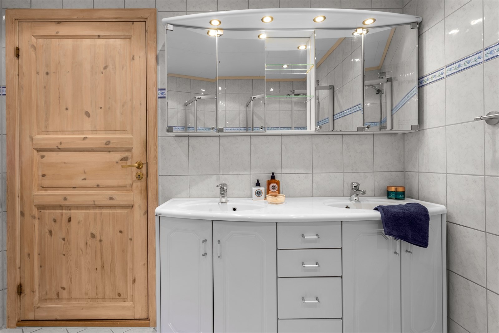 Badet er utstyrt med dusjhjørne med glassvegger/dør og dobbel servant på baderomsinnredning med praktiske speilskap. Galleribilde