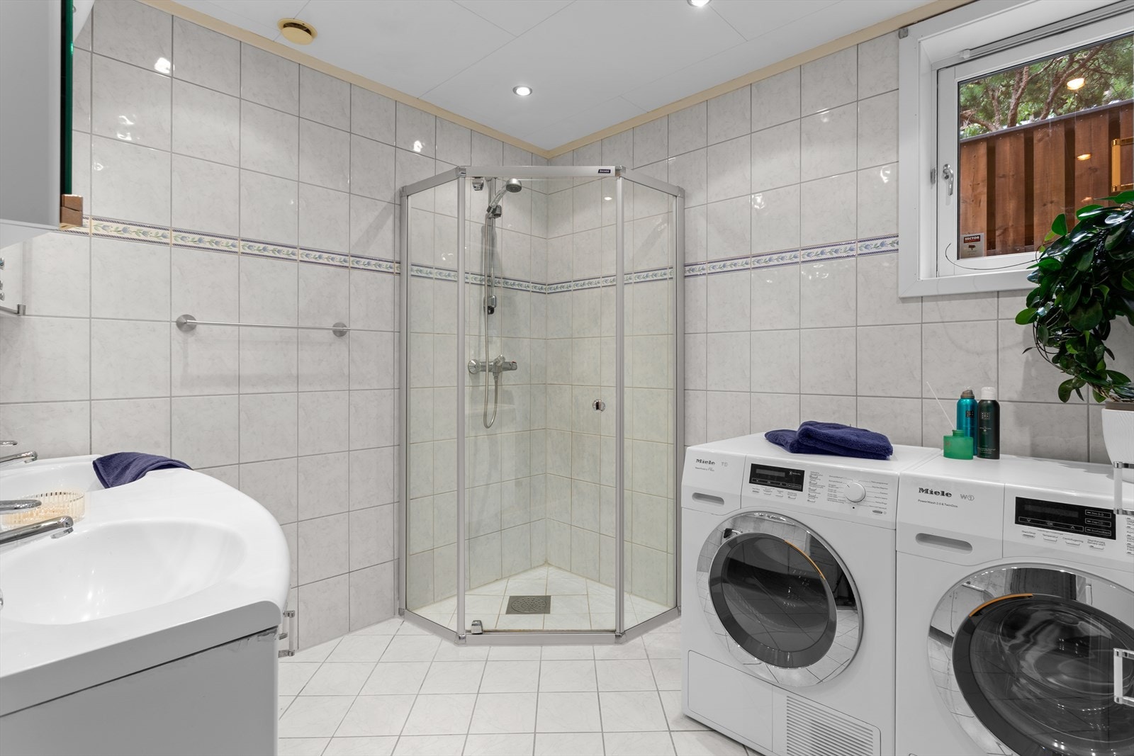 Flislagt baderom med varmekabler i gulv og downlights i himling. Rommet kombineres som vaskerom og har plass med opplegg til vaskemaskin og tørketrommel. Galleribilde