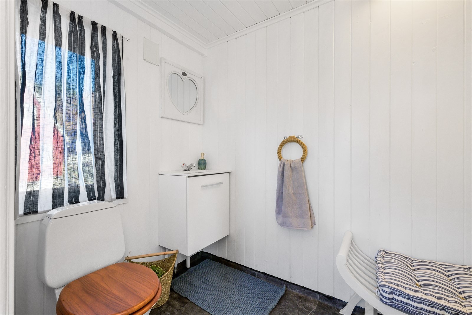 Praktisk toalettrom utført med våtromsbelegg på gulv og malt trepanel på veggflater. Det inneholder servant m/undeskap og toalett. Toalettrommet har opplegg for vaskemaskin. Galleribilde