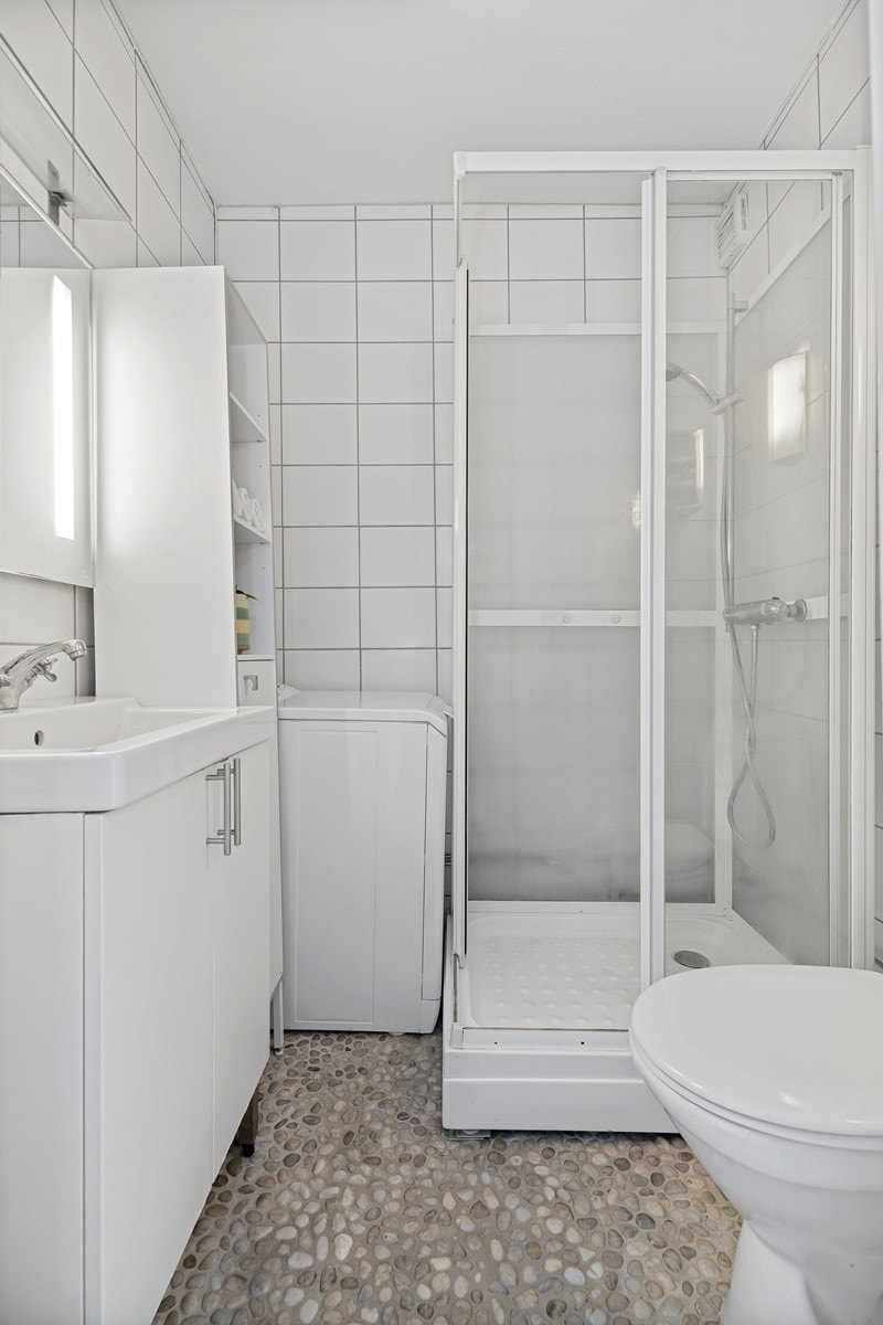 Flislagt bad med toalett, dusjkabinett, servant, høyskap og opplegg til vaskemaskin. Galleribilde