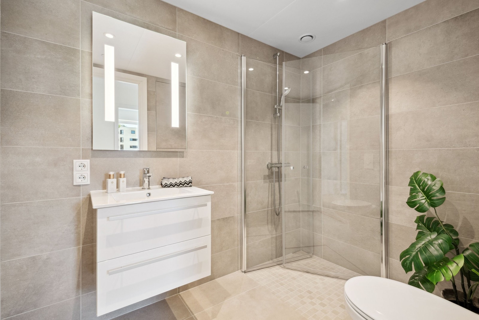 Helfliset delikat baderom med moderne overflater og opplegg for vaskemaskin. Downlights i taket og vegghengt toalett. Galleribilde