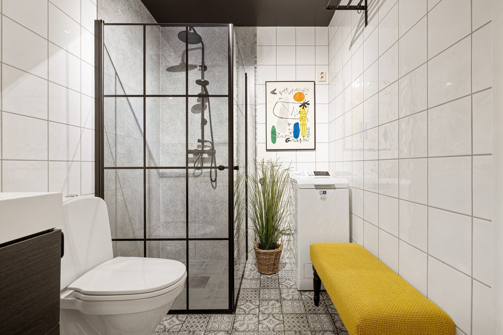 Dusjhjørne med innfellbare glassdører og sort armatur med både hånd- og regnfallsdusj. Baderommet er også utstyrt med gulvstående toalett og opplegg for vaskemaskin. Galleribilde