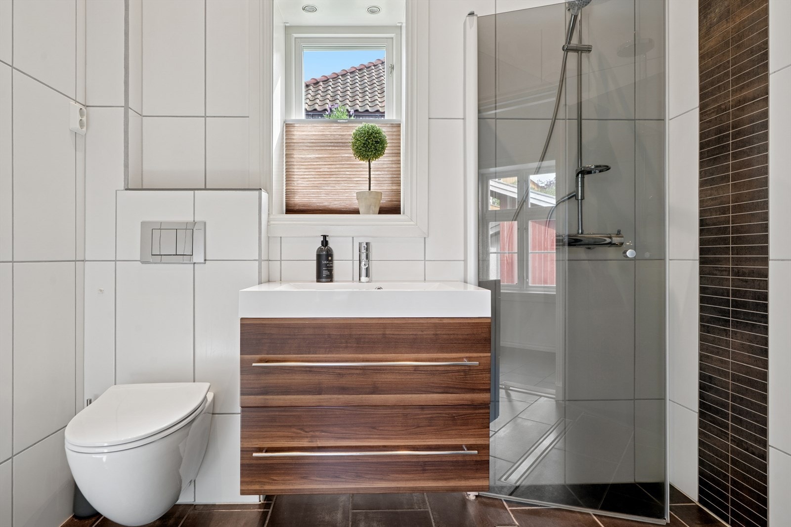 Praktisk baderom i tilknytning til entréen, innredet med vegghengt toalett, skuffeinnrending med overliggende servant og dusjhjørne med innfellbare dusjdører Galleribilde