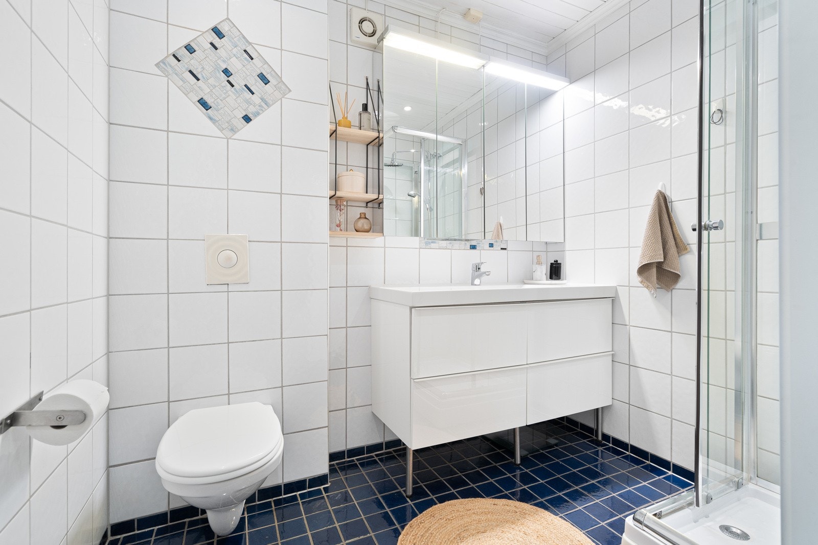 Badet er utstyrt med vegghengt toalett, baderomsinnredning og dusjkabinett. Galleribilde