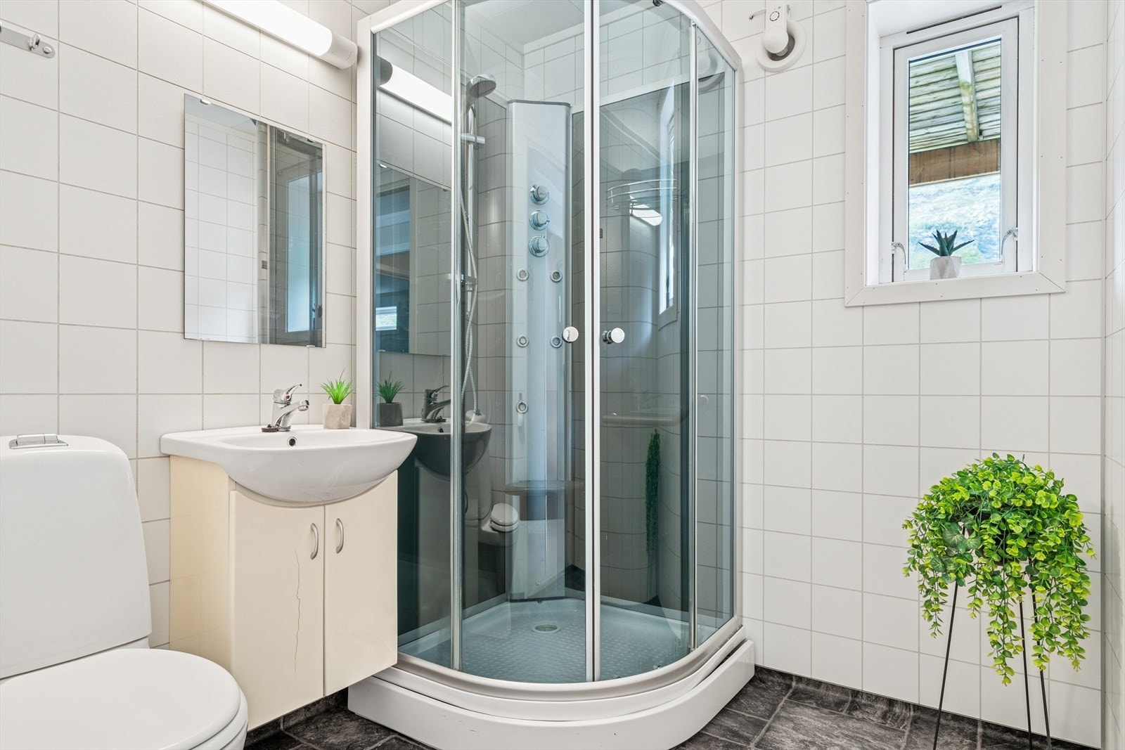 Bad i underetasje har vinylbelegg på gulv med varmekabler og baderomsplater på vegger. Badet er utstyrt med gulvmontert toalett, dusjkabinett, baderomsinnredning med servant. Galleribilde