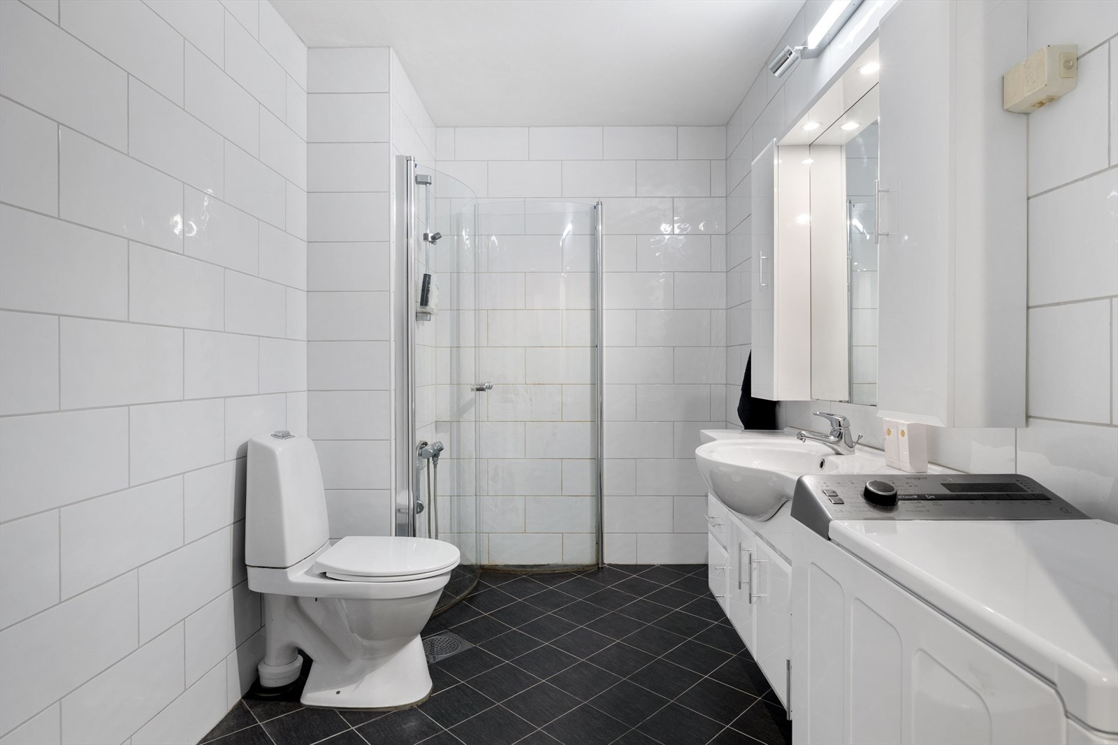 Pent helfliset bad med baderomsinnredning, nedsenket servant, toalett, dusjhjørne og plass til vaskemaskin Galleribilde