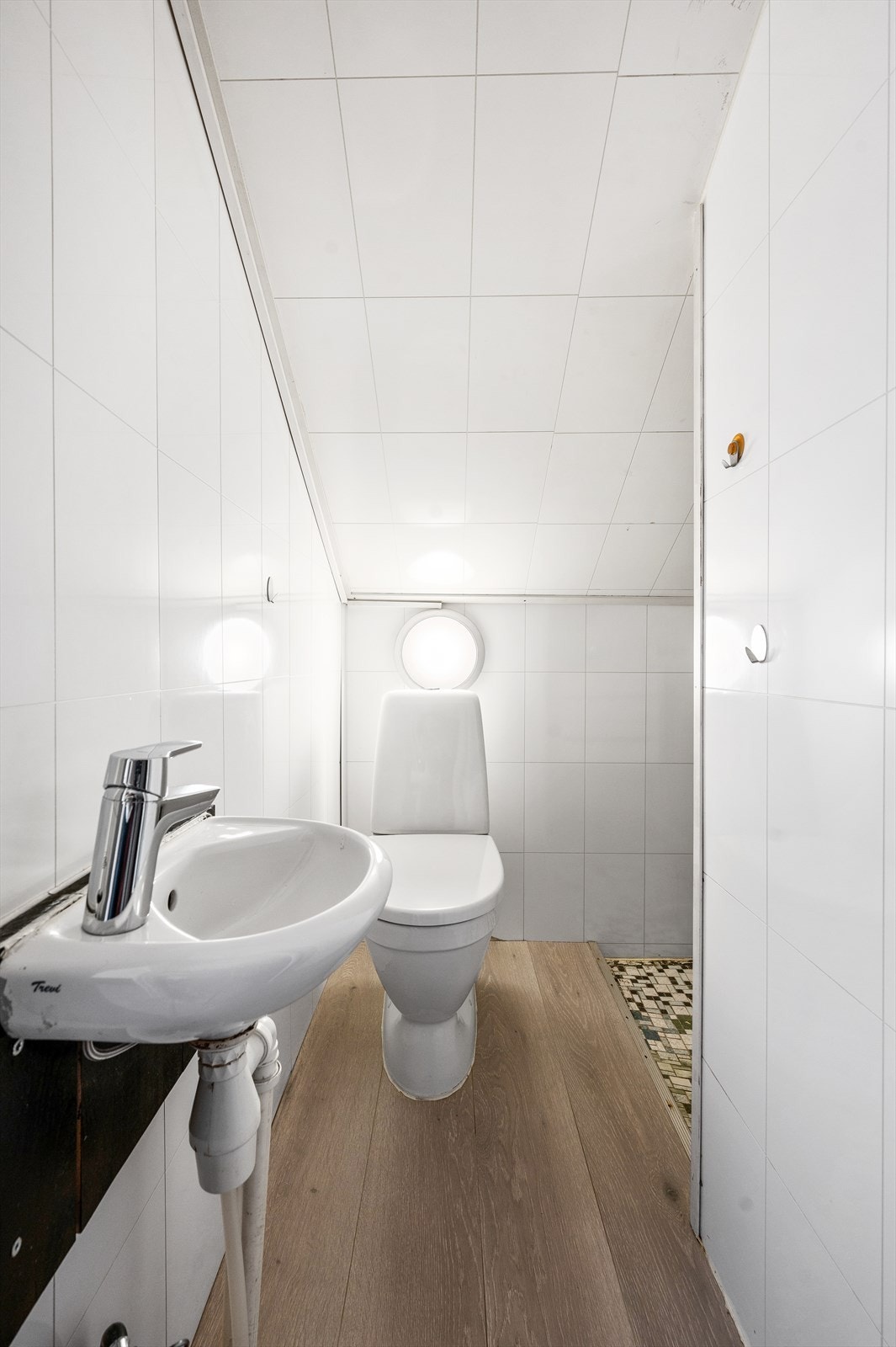 Badet har våtromsplater på vegg, laminat og fliser på gulv, og er innredet med servant, speil, belysning og klosett. Badet må påregnes oppussing. Lav takhøyde. Galleribilde