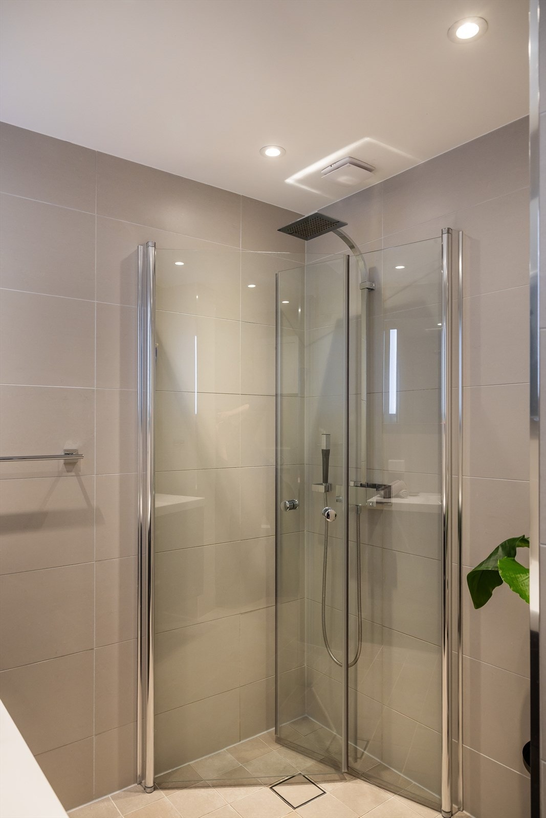 Baderom har flislagt gulv og veggflater og er innredet med servant/skap, veggmontert toalett og dusjhjørne med innfellbare glassdører. Galleribilde