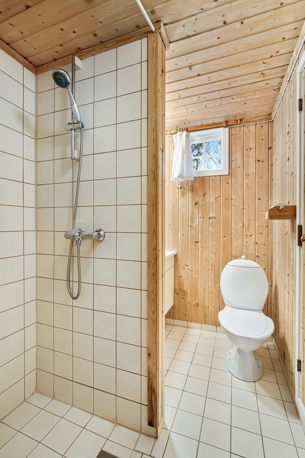 Badet i den nordre delen har flislagt gulv og dusjnisje, paneloverflater, toalett og hvit innredning. Galleribilde