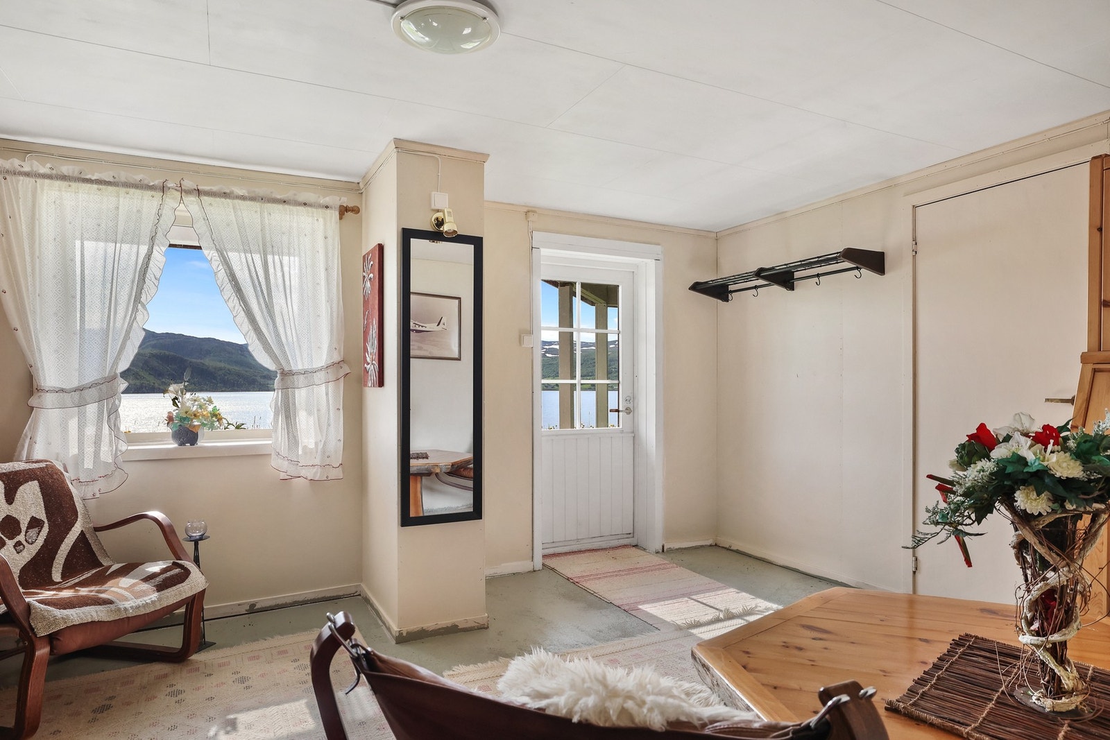 Lyst hjørnerom med enkel innredning og utgang til overbygd uteplass. Utsyn over vann og åser gir rommet en åpen og tilbaketrukket karakter. Galleribilde