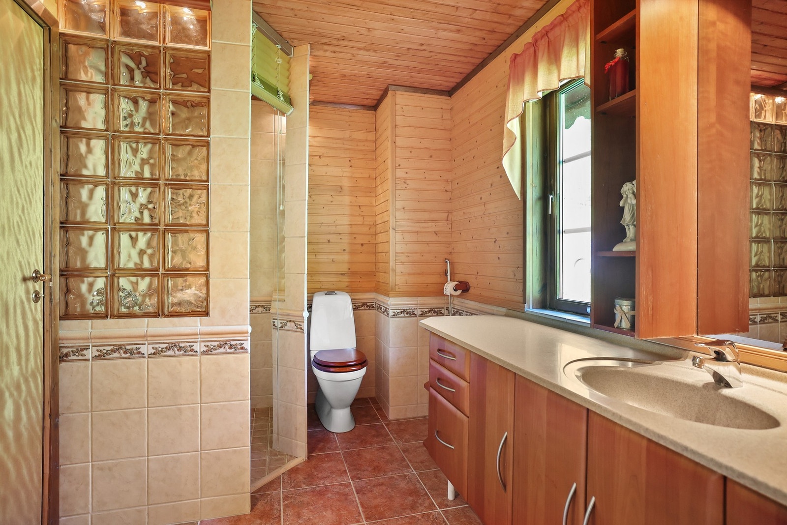 Badet har flislagte overflater og heltrepanel og innredning i varme trefarger. Galleribilde