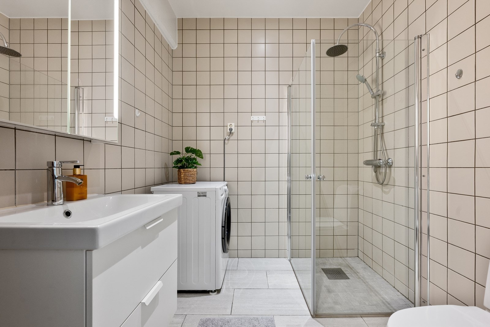 Badet er fra byggeår har flislagte overflater med varme i gulv - Badet er romslig og har god plass til benkeskap, servant, veggskap med speilfront og belysning, dusj med innfellbare dører i herdet glass, gulvstående wc og opplegg for vaskemaskin Galleribilde