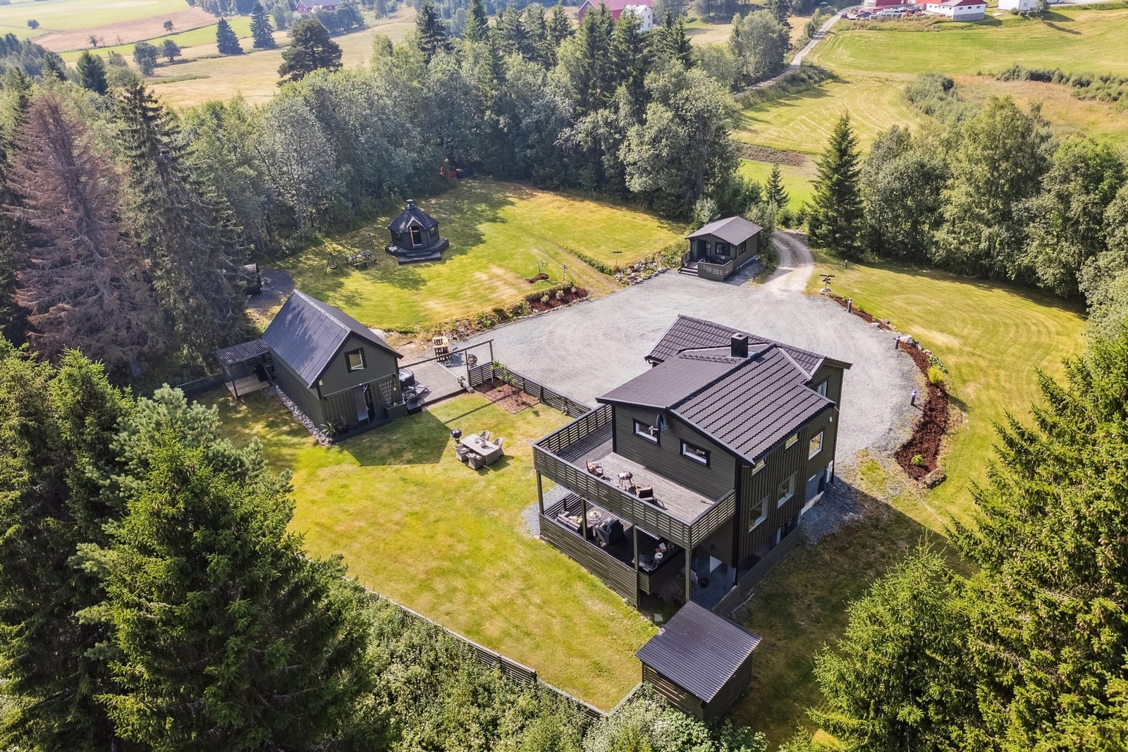 Balkongen strekker seg langs flere sider av boligen. Eiendommen har en svært romslig og gruslagt parkeringsplass som omkranses av plen, beplantning og stemningsfull belysning. Galleribilde