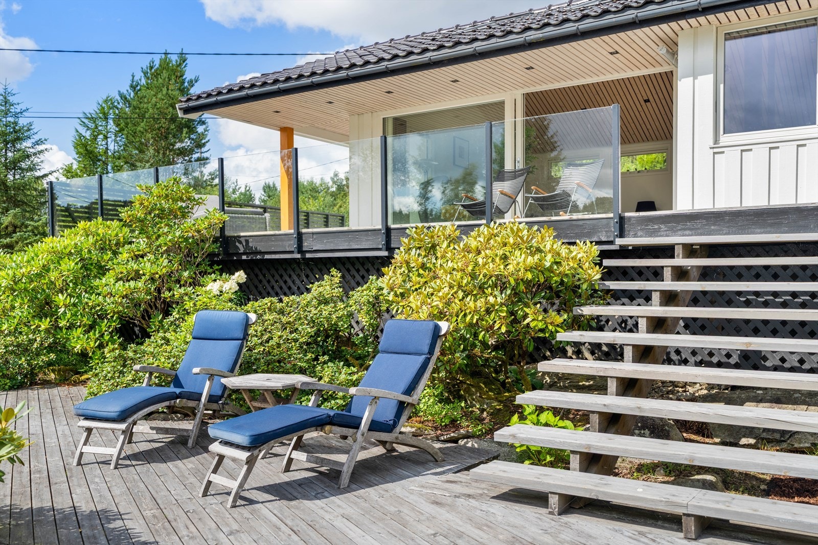 Moderne terrasse med glassrekkverk, overbygg og omgitt av frodig natur Galleribilde