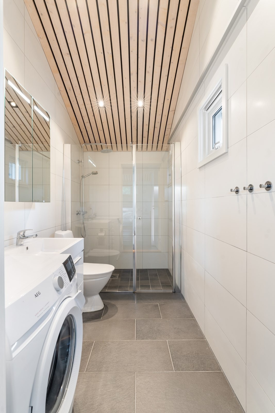 Den stilfulle innredningen inkluderer en nedfelt servant, toalett og en praktisk dusjvegg, i tillegg til opplegg for vaskemaskin som gjør rommet ekstra funksjonelt Galleribilde