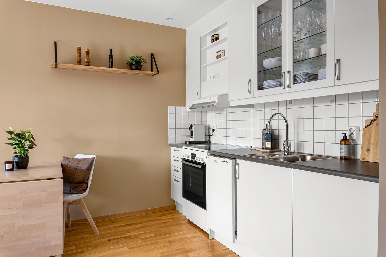 Innredningen har hvite fronter og mørke detaljer over benk, samt frittståenede komfyr og oppvaskmaskin. Galleribilde