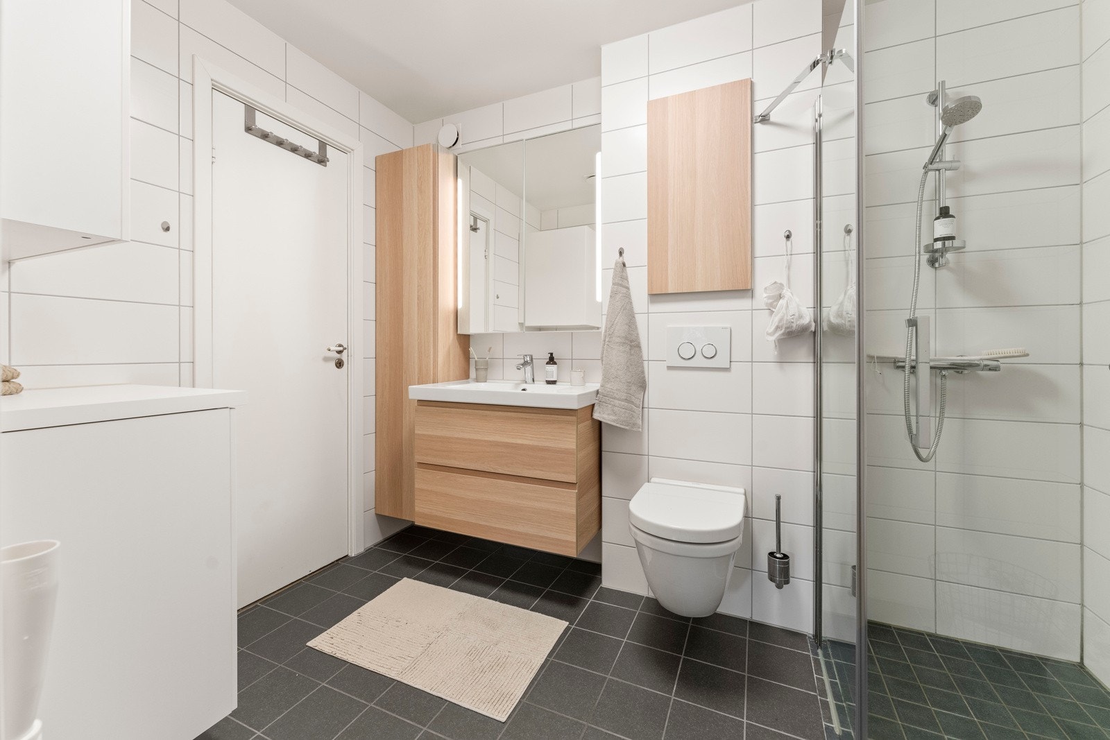 Badet ble oppgradert for ca. 10 år siden og fremstår som romslig og moderne, med fliser på vegger og gulv, dusjnisje med glassdører, vegghengt toalett og praktisk innredning med god skapplass og opplegg for vaskemaskin. Galleribilde