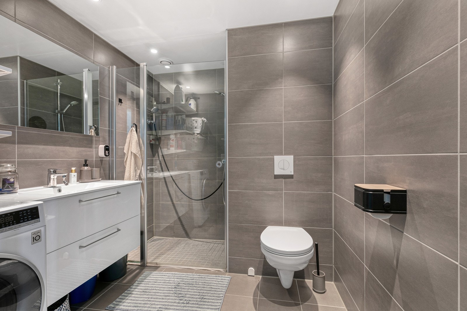 Delikat flislagt baderom. Inneholder dusjnisje, servantinnredning, wc og opplegg til vaskemaskin. Galleribilde