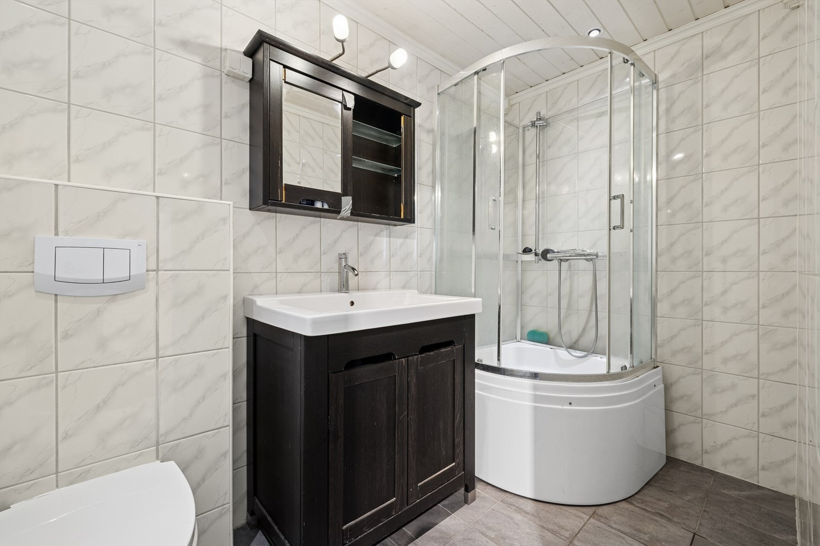 Badet i første etasje er helfliset og består av speilskap, servant med seksjon, veggmontert toalett og dusjkabinett. Galleribilde