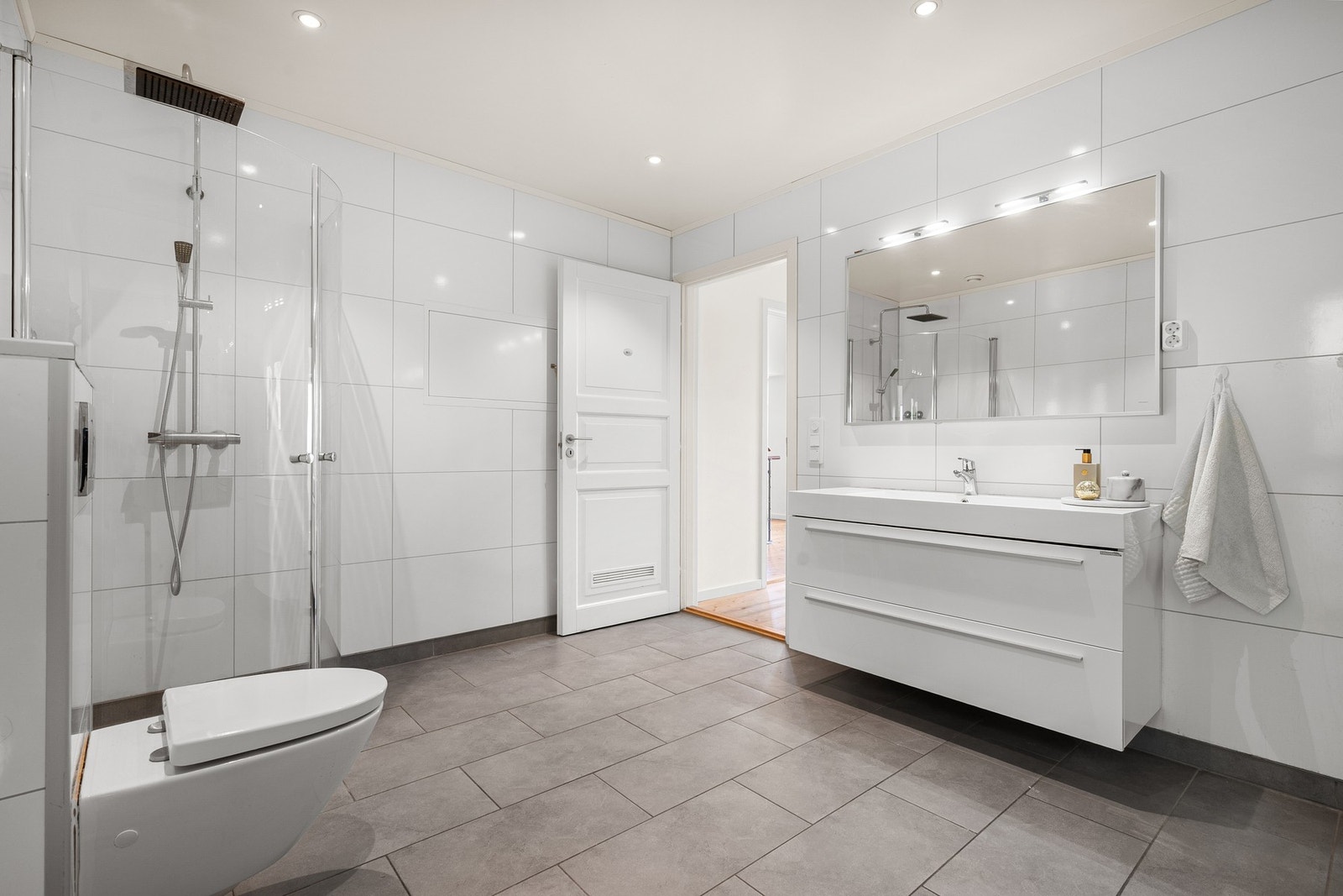 Videre inneholder badet servantinnredning, toalett og dusjhjørne med glassdører og regndusj Galleribilde