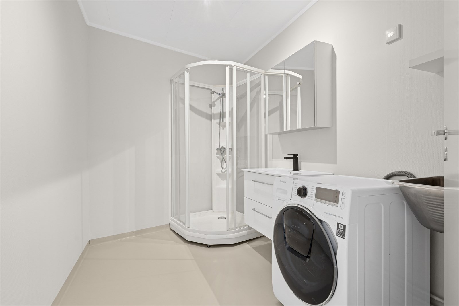 Badet inneholder dusjkabinett, opplegg for vaskemaskin/tørketrommel, utslagsvask og servantinnredning. Galleribilde