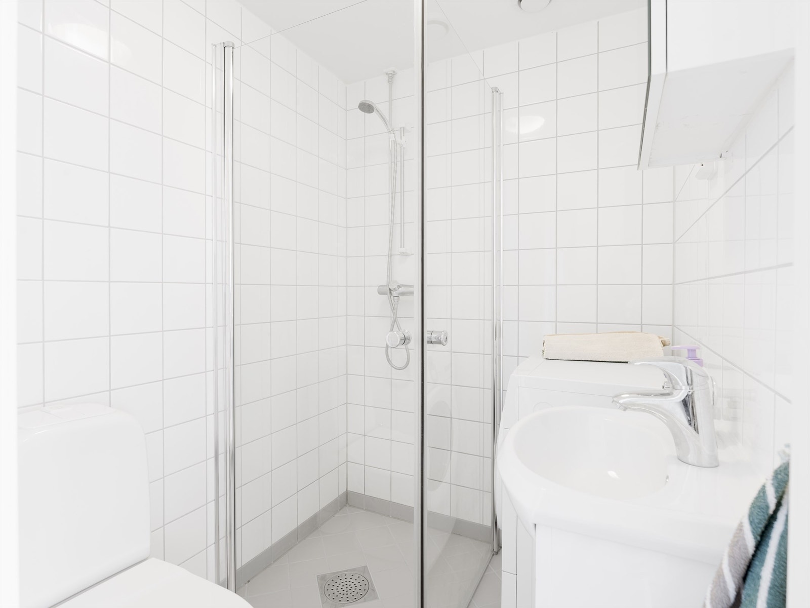 Romslig bad fra 2010 med dusjdører i glass, servant m/ overskap, toalett og opplegg for vaskemaskin. Galleribilde