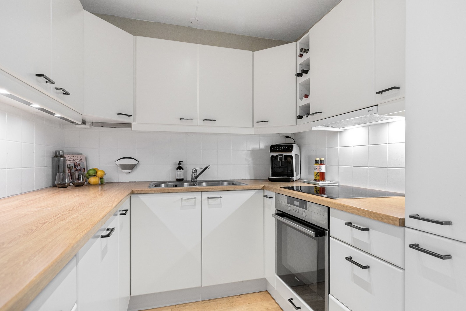 Vegg over benkeskap har overflate med flisetterligning, og benkeplaten er i laminat. Galleribilde