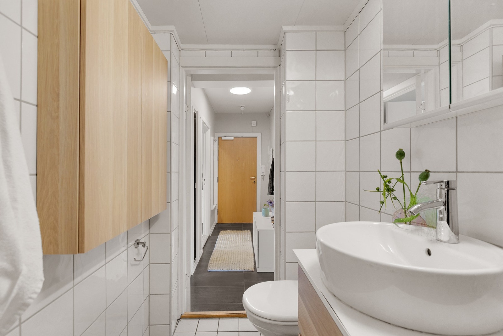 Badet er innredet med toalett, dusjhjørne med innfellbare glassdører, vegghengt servantinnredning med ovenpåliggende servant og speilskap med overlys og stikkontakt. Galleribilde