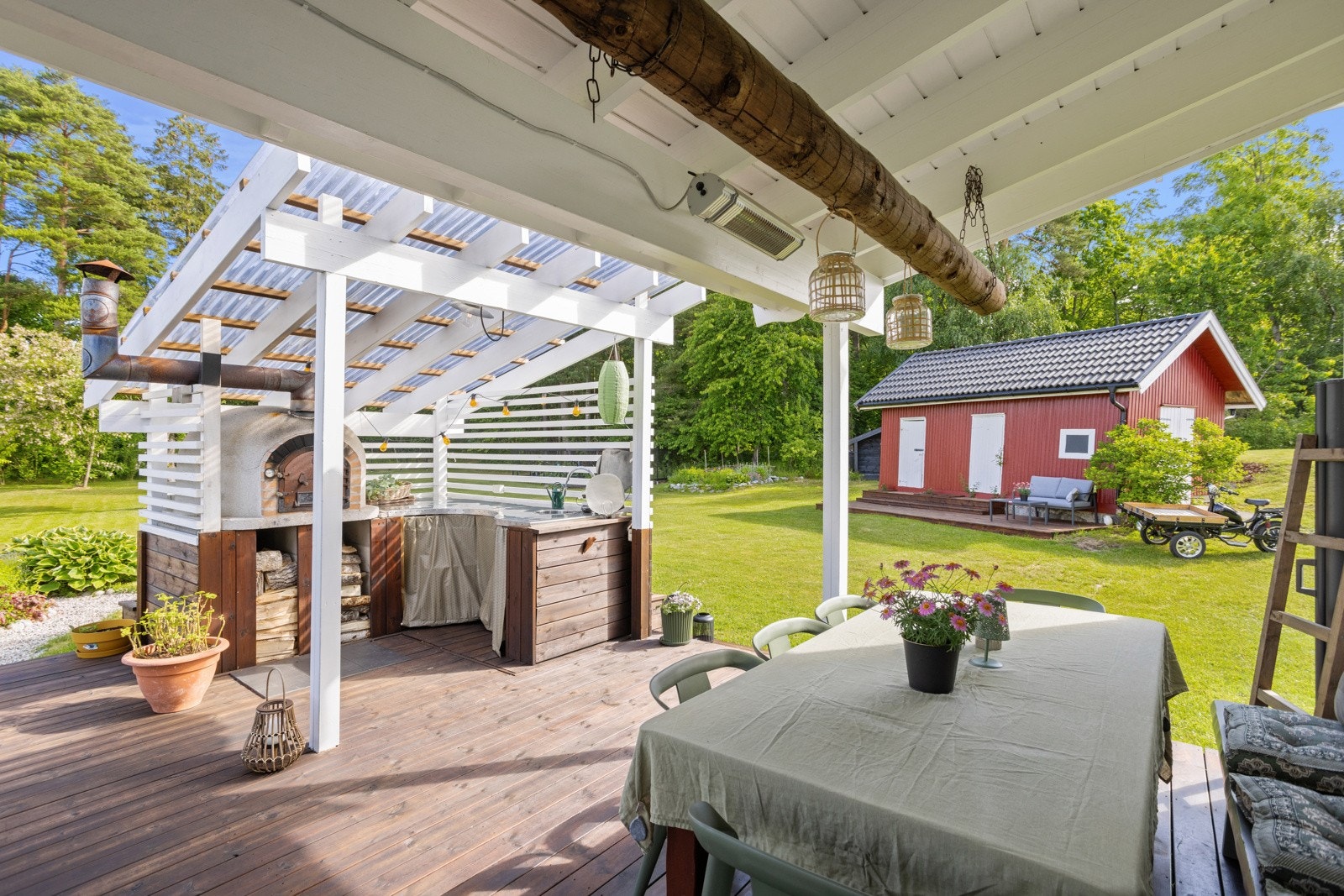 Under pergolaen har terrassen et flott utekjøkken med vaskekum, arbeidsbenk og vedfyrt ovn for matlaging Galleribilde