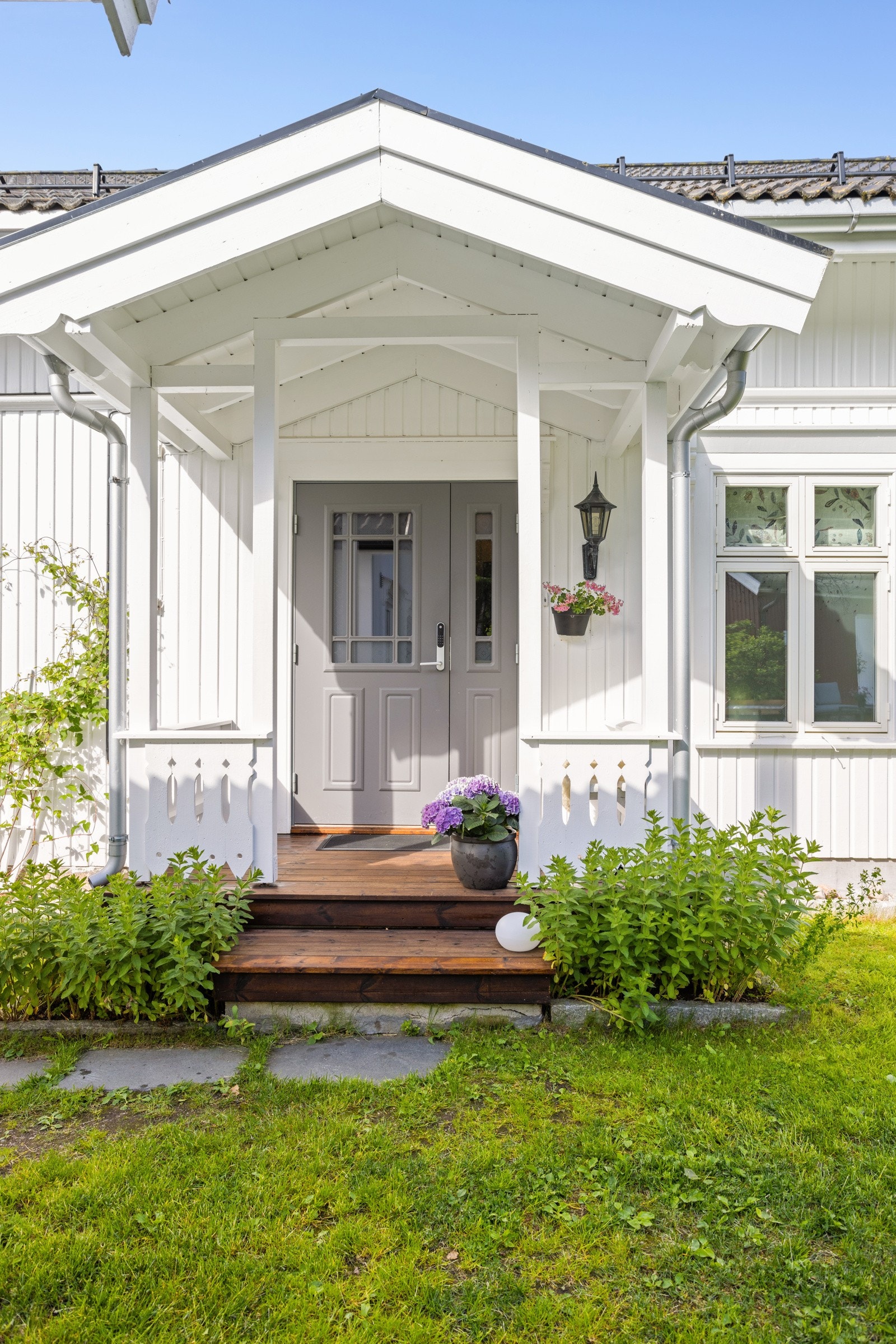 Et overbygd inngangsparti ønsker velkommen, med utskjæringer, belysning og en vakker ytterdør fra 2012. Galleribilde