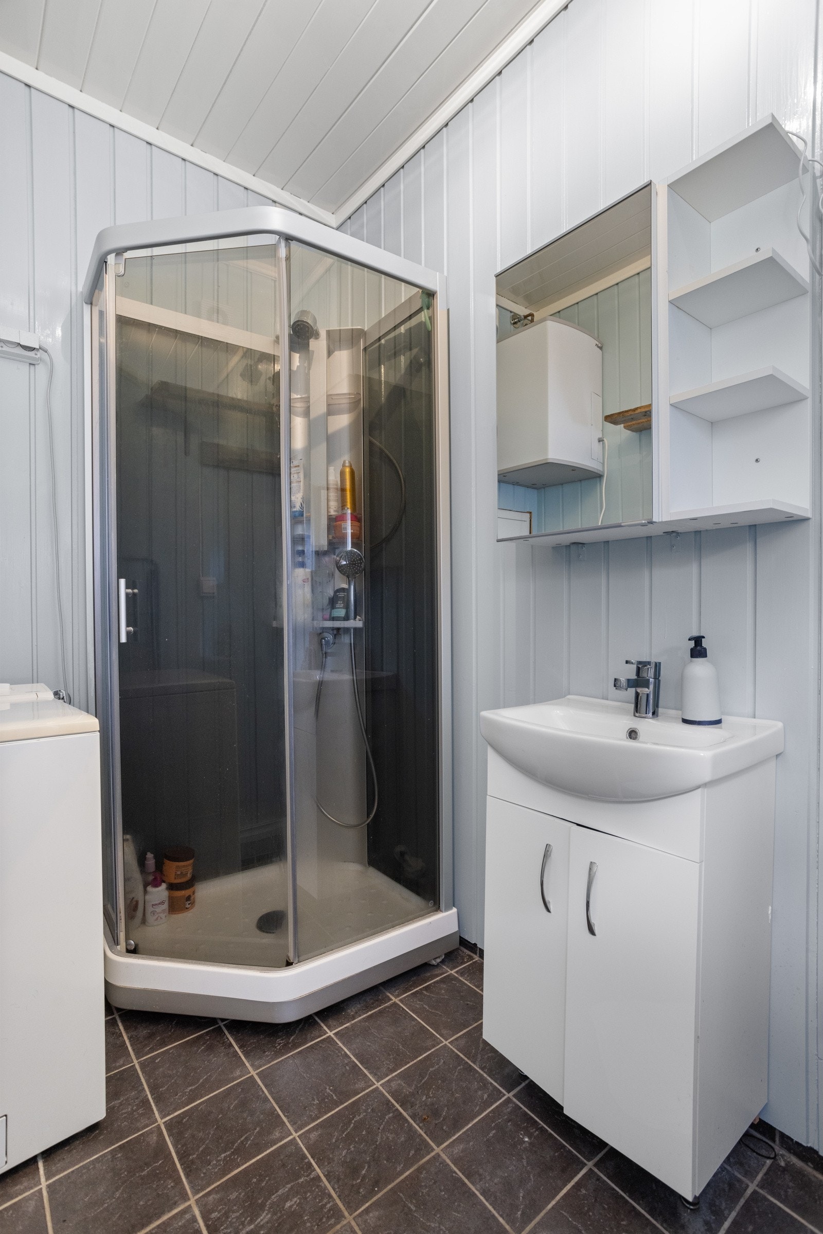 Badet har flislagt gulv, lyse panelvegger og et hvitt servantskap med tilhørende speilskap. På badet er det toalett, varmekabler og dusjkabinett, og i 2023 ble det installert en ny, elektrisk vifte Galleribilde