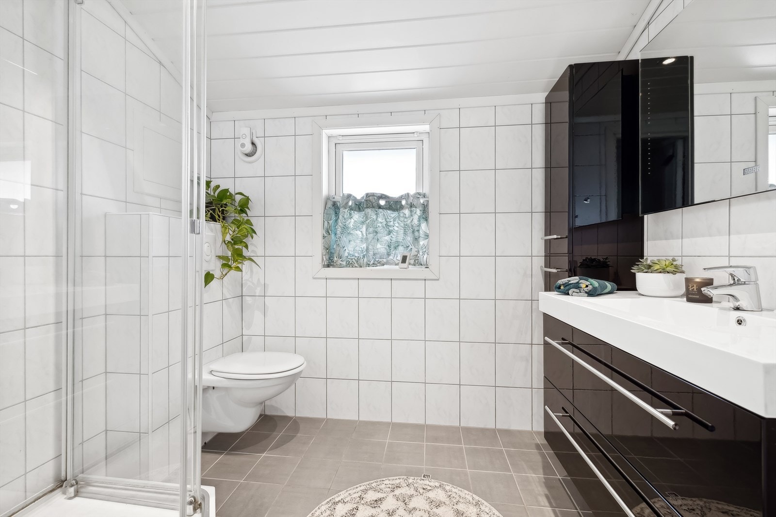 Badet har dusjkabinett, servant med moderne innredning og skuffer, speil med innfelt lys, høyskap og vegghengt toalett. Galleribilde