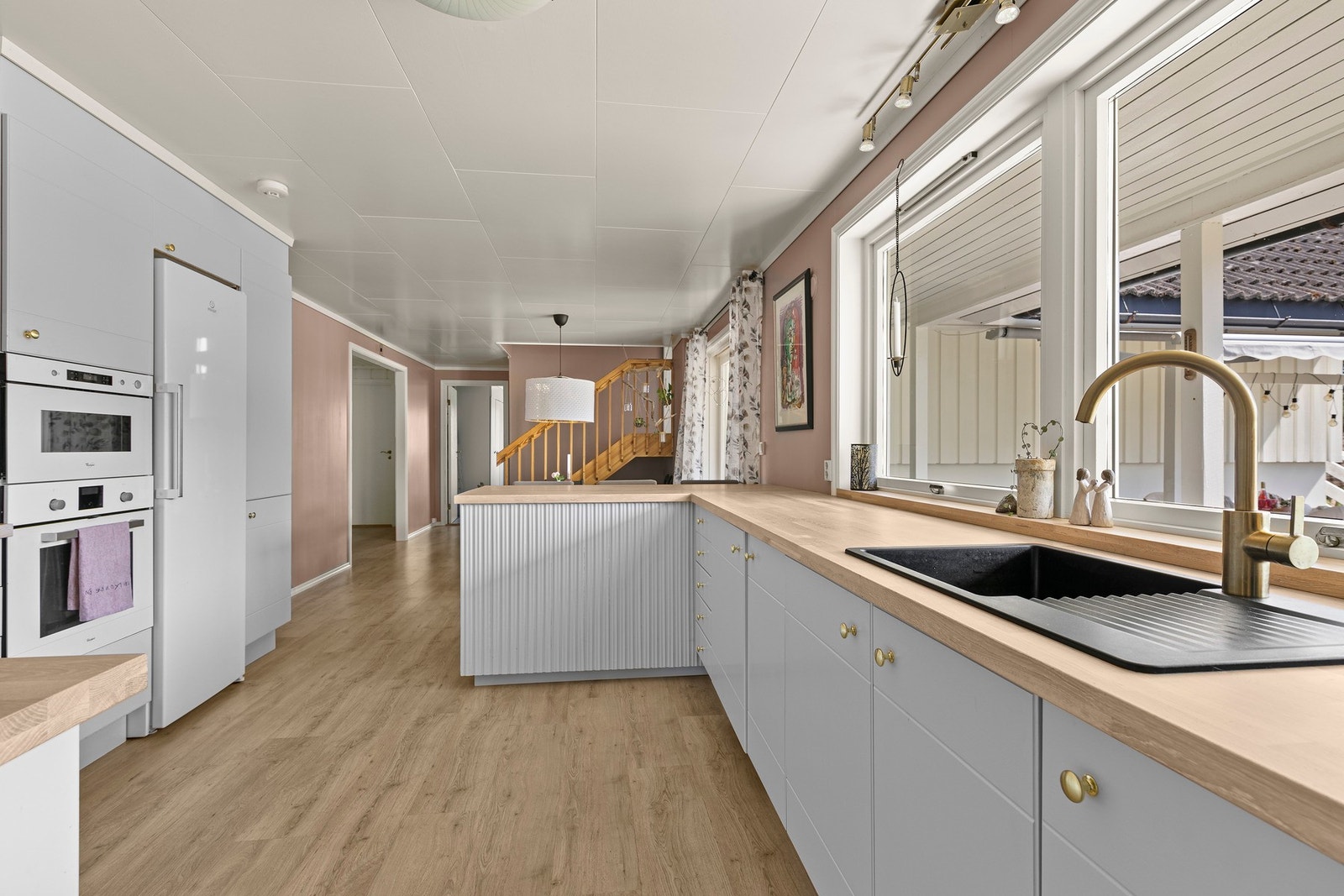 Kjøkkenet i hoveddelen har et stilfullt og moderne design med langstrakte benkeflater og rikelig med oppbevaringsplass. Innredningen har lysegrå, glatte fronter, takhøye skap og pen benkeplate med nedfelt, sort kum. Veggene over benken er kledd med lyse f Galleribilde