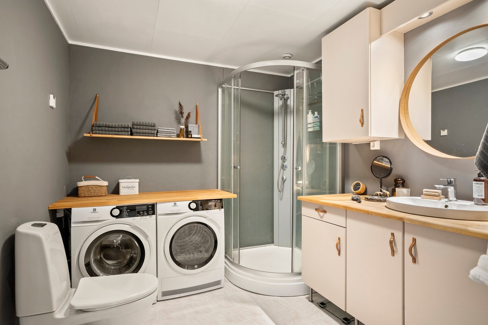 Badet er utstyrt med dusjkabinett, servantseksjon med skuffer og heldekkende porselensvask, speil med lys, gulvmontert wc og opplegg for vaskemaskin/tørketrommel. Galleribilde