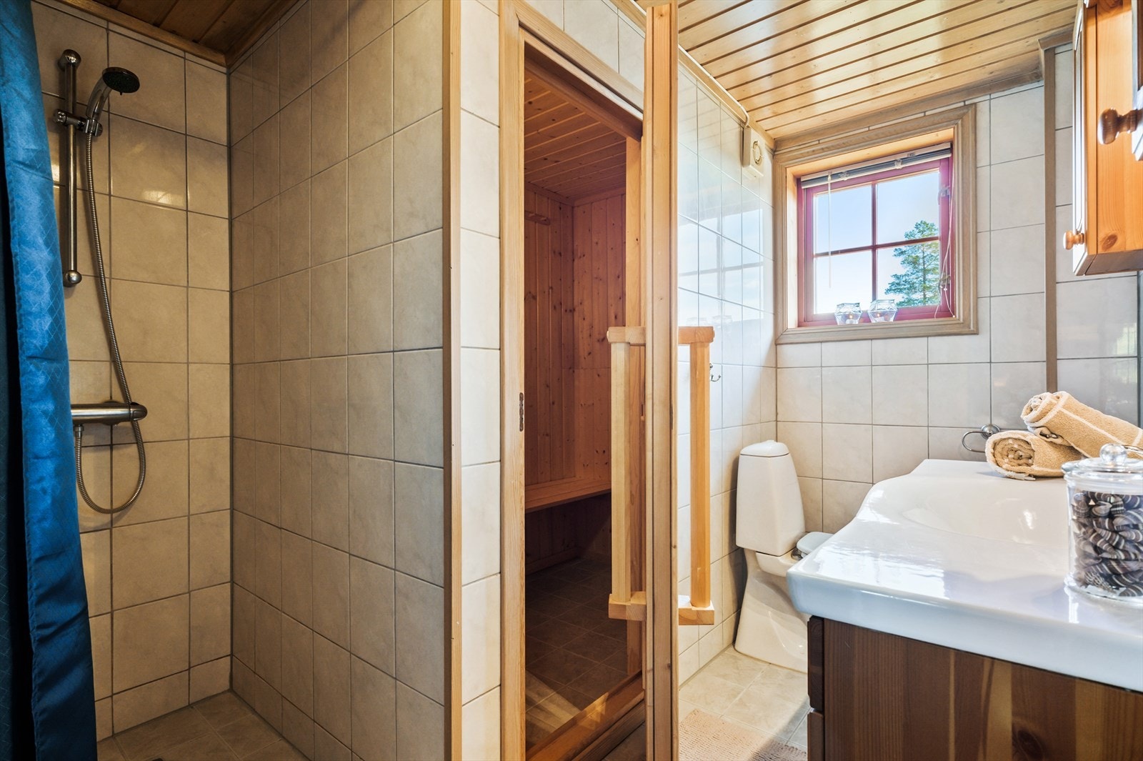 Lyst og pent bad med flislagte gulv og vegger, og himling med panel. Badet er innredet med heldekkende servant nedfelt i romslig benkeskap, overskap og belyst speil, frittstående toalett og dusjnisje.
Varmekabler i gulv og direkte adkomst til badstue. Galleribilde
