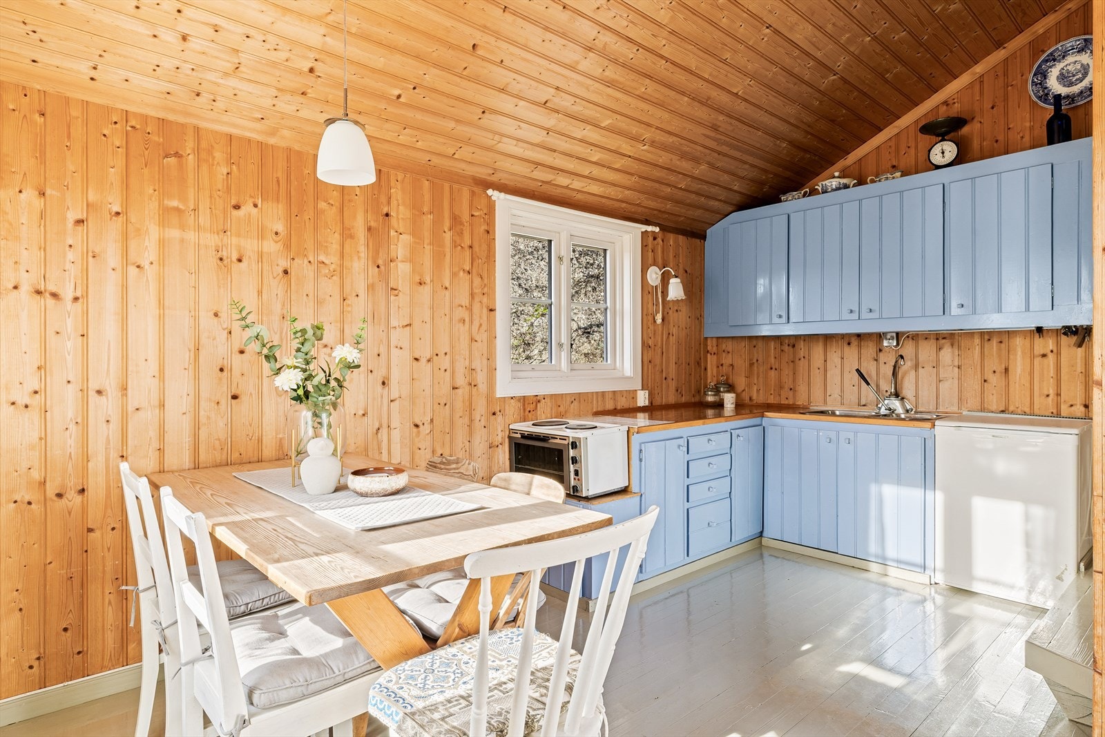 Den lyseblå kjøkkeninnredningen står fint til det naturlige panelet på veggene. Galleribilde