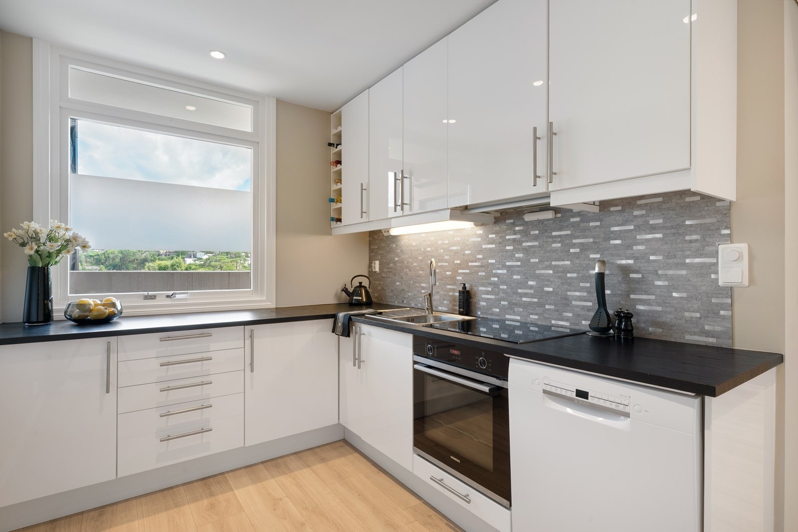 Ikea kjøkkeninnredning med laminert benkeplate. Slette fronter. Opplegg for oppvaskmaskin og amerikansk kjøleskap. Integrert stekeovn og platetopp. Plater med flisemønster mellom benkeplate og overskap. Galleribilde